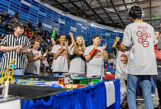 Referee and team of cheering students around a FIRST LEGO League game table