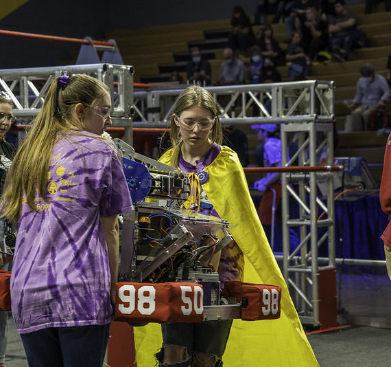 Two teenage women lift a robot onto the playing field